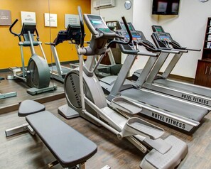 Gimnasio de hotel con cintas de correr, elípticas y una banca.