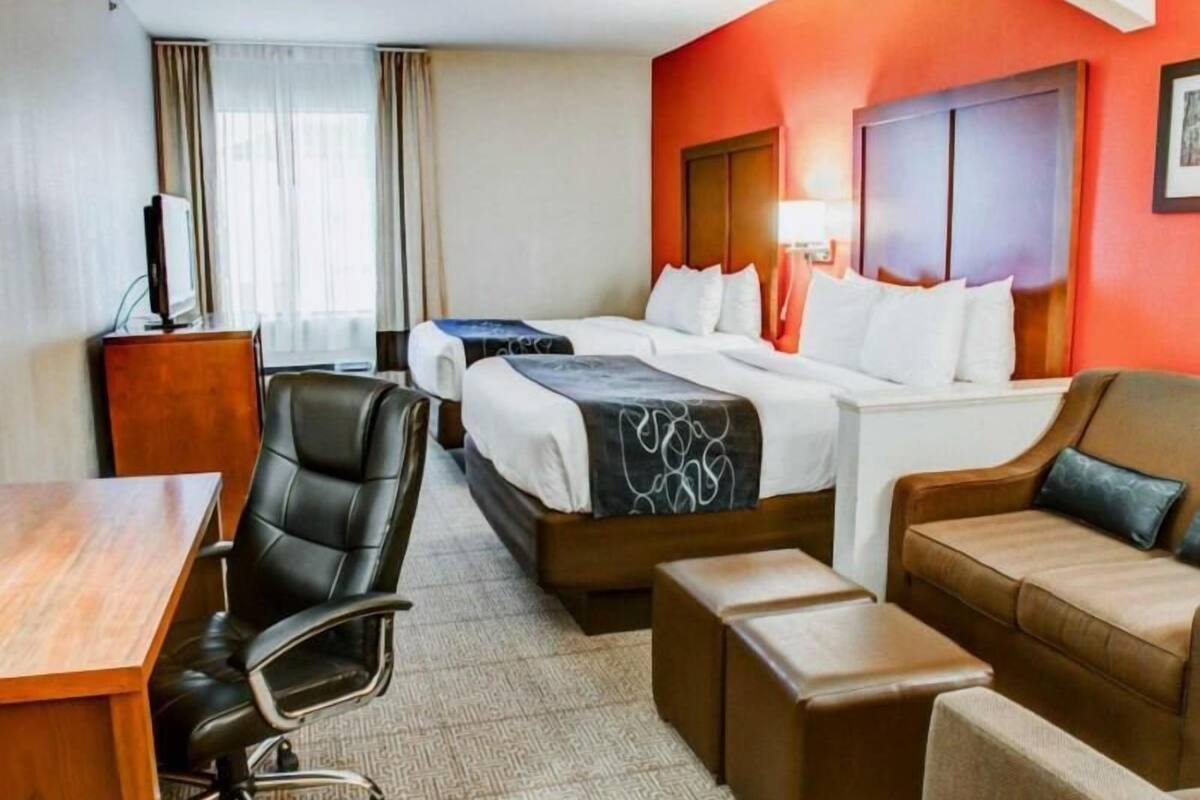A hotel room with two beds, a desk, a chair, a sofa, and a TV.