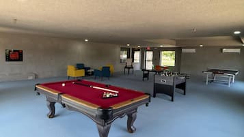 A recreational room with a pool table, foosball table, and several chairs.