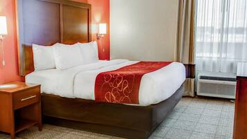 A hotel room with a large bed, a nightstand, a wall-mounted lamp, and a window with curtains.