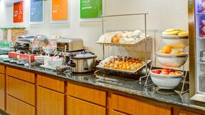 A buffet counter with various food items, a coffee station, and a refrigerator.