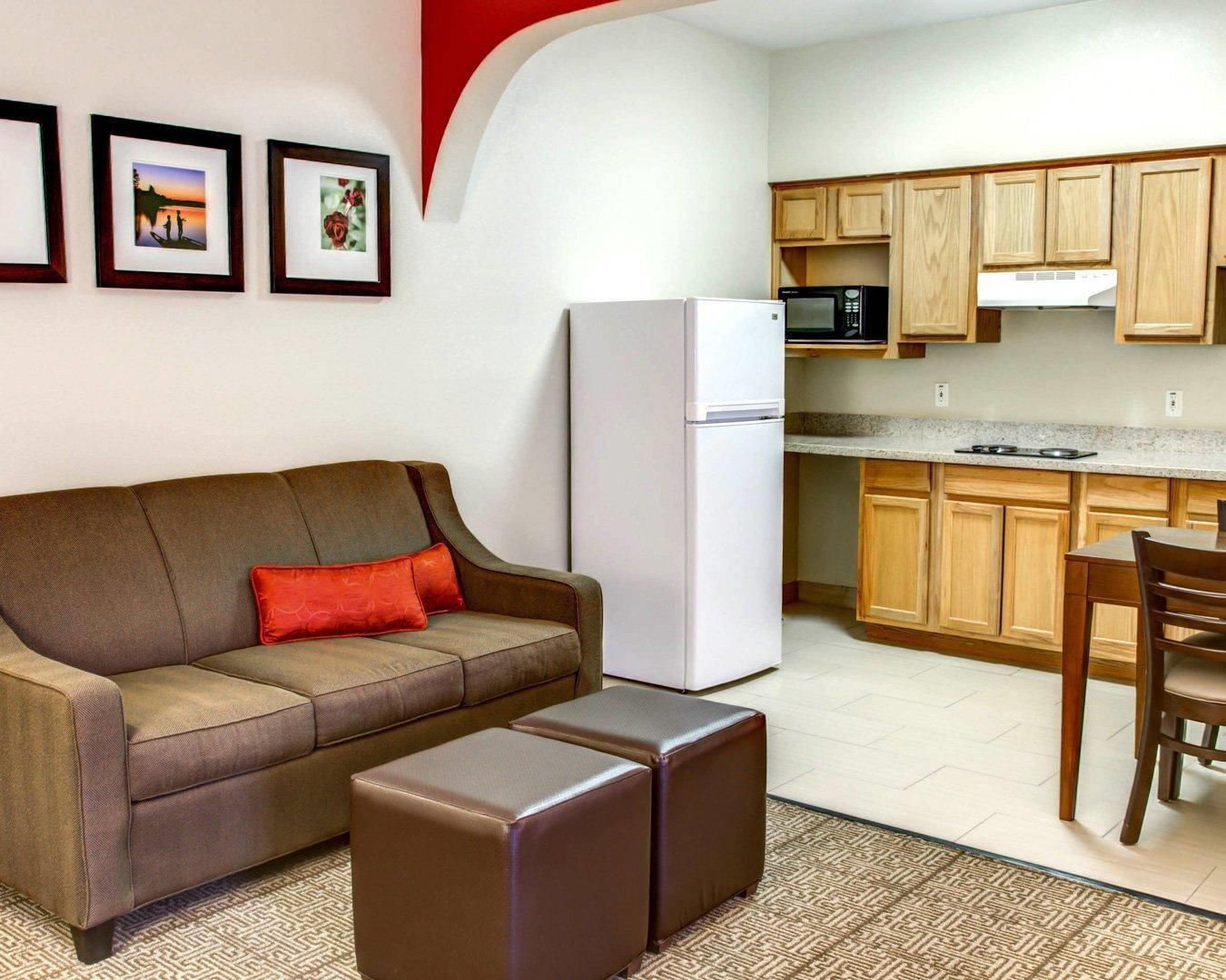 Una sala de estar con sofá, otomanas, un refrigerador y un microondas en una cocina pequeña.
