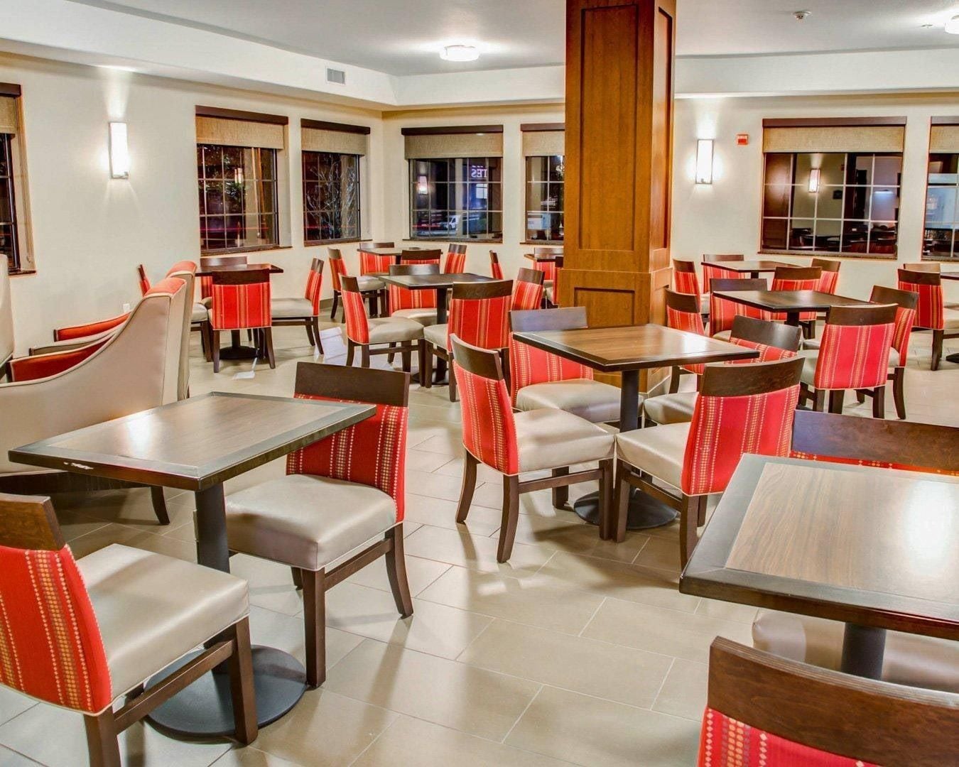 A restaurant with multiple tables and chairs, a wooden pillar, and large windows.