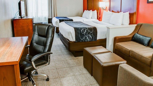 A hotel room with two beds, a desk, a chair, and a sofa.