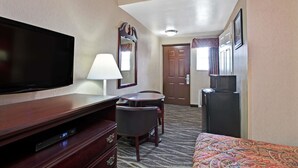 A hotel room with a flat-screen TV, a desk with a lamp, a chair, a bed with a patterned bedspread, and a refrigerator. - Days Inn by Wyndham Ridgefield NJ (Ridgefield)