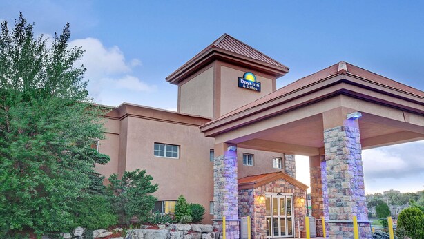 A Days Inn & Suites with a stone entrance, a clear sky, and surrounding greenery. - Days Inn by Wyndham Ridgefield NJ (Ridgefield)