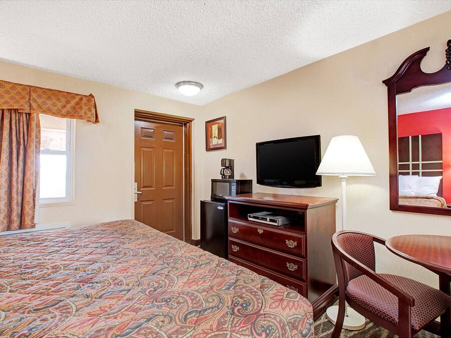 Habitación de hotel con una cama grande, un escritorio con silla, televisor, lámpara y microondas.