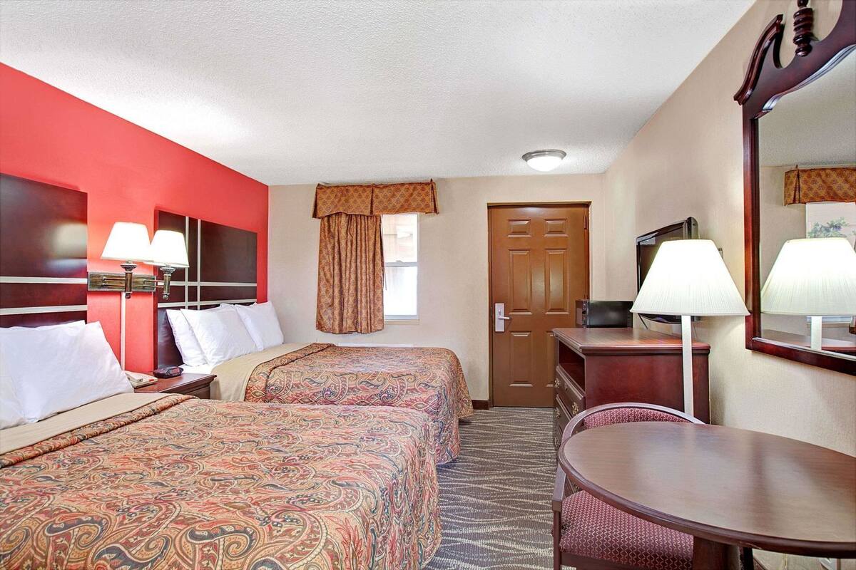 Une chambre d’hôtel avec deux lits, un bureau, une chaise, une télévision et une porte.