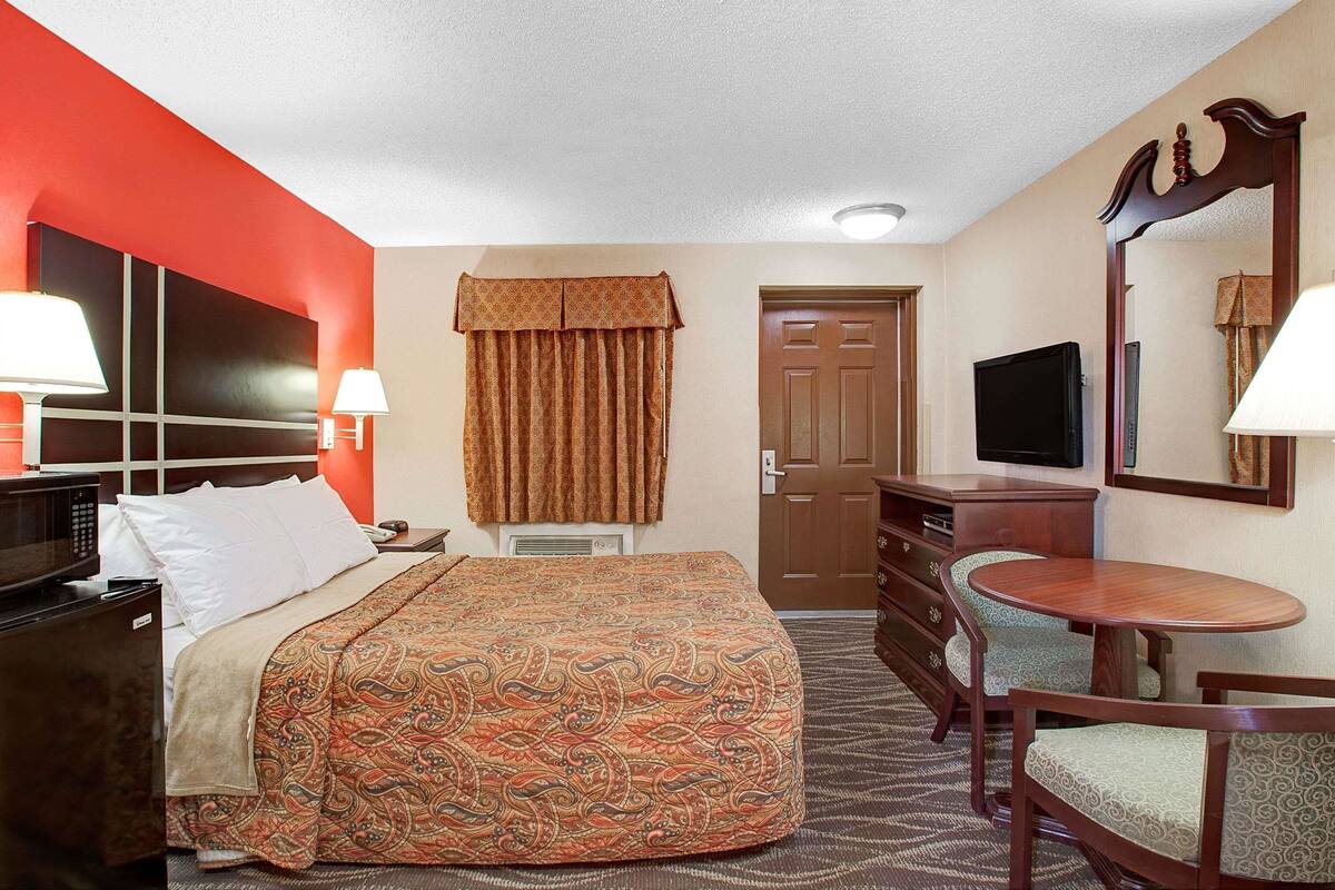 Une chambre d’hôtel équipée d’un lit, d’un bureau, d’une chaise, d’une télévision et d’un miroir.
