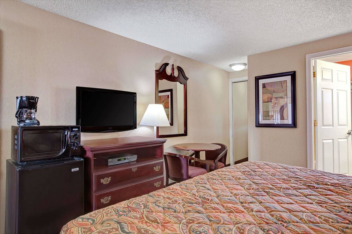 Une chambre d’hôtel équipée d’un lit, d’une télévision, d’une machine à café, d’une commode, d’une lampe et d’un tableau encadré au mur.