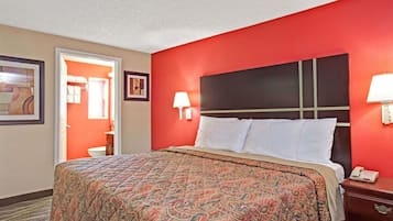 A hotel room with a large bed, red walls, a white headboard, and a bedside table with a lamp.