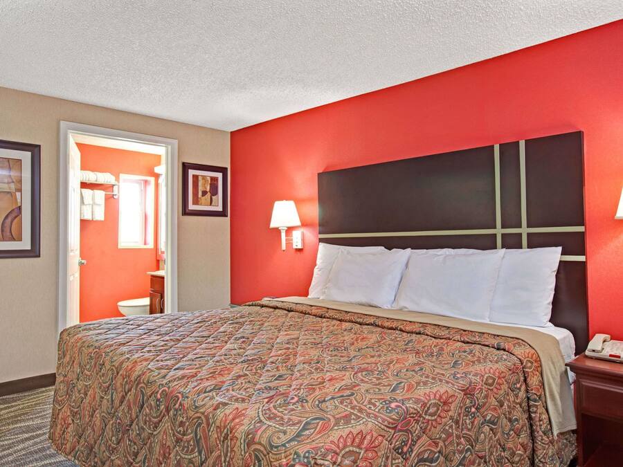 A hotel room with a large bed, red walls, a white headboard, and a bedside table with a lamp.