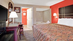 A hotel room with a bed, a desk with a lamp, a television, and a bathroom visible through an open door. - Days Inn by Wyndham Ridgefield NJ (Ridgefield)