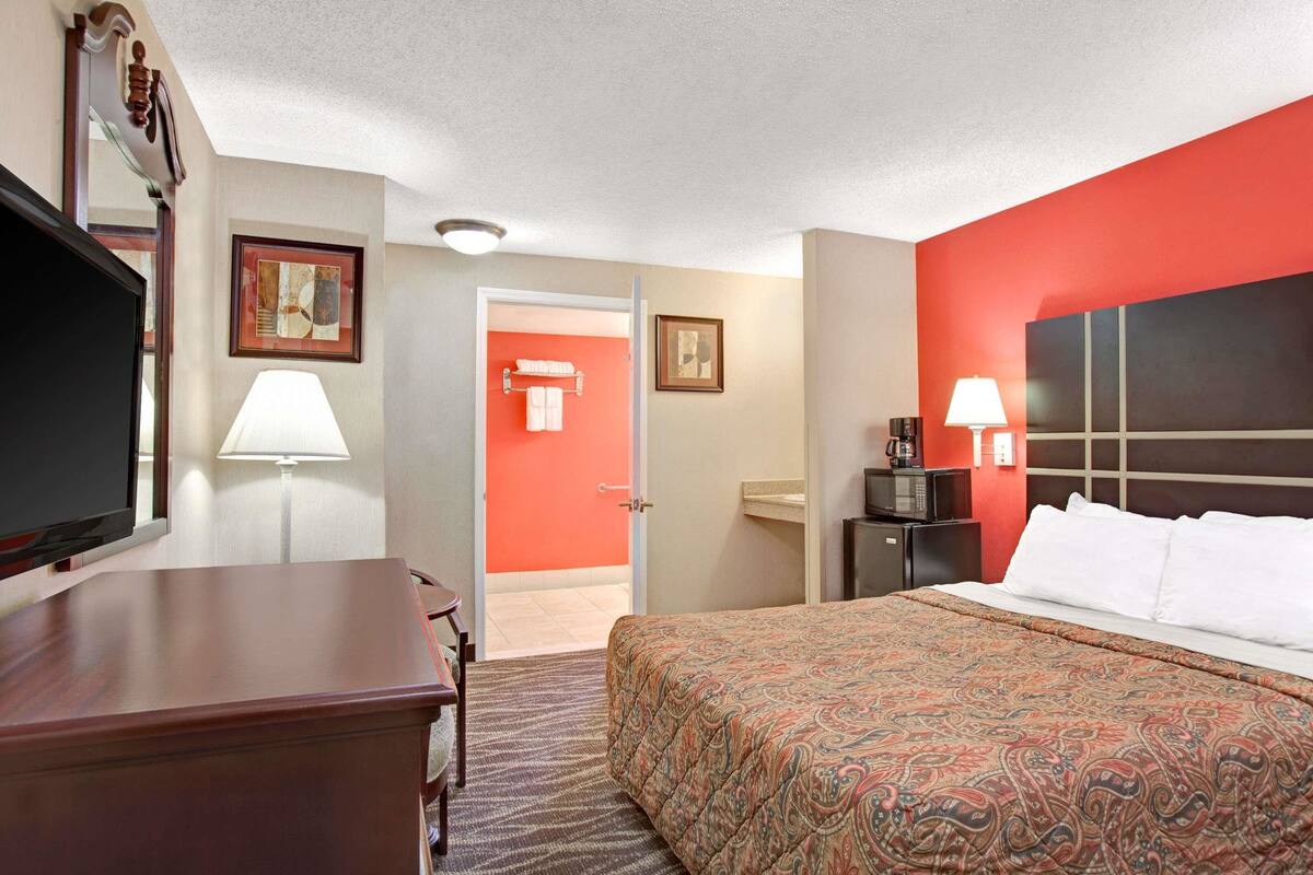Une chambre d’hôtel avec un grand lit, un bureau, une télévision et une salle de bain visible à travers une porte ouverte.