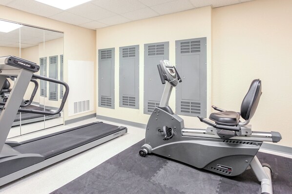 Un gimnasio con cintas de correr, elíptica y un espejo grande.