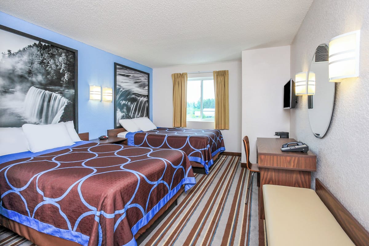 Een hotelkamer met twee bedden, een bureau, een stoel, een televisie en een raam met gordijnen.