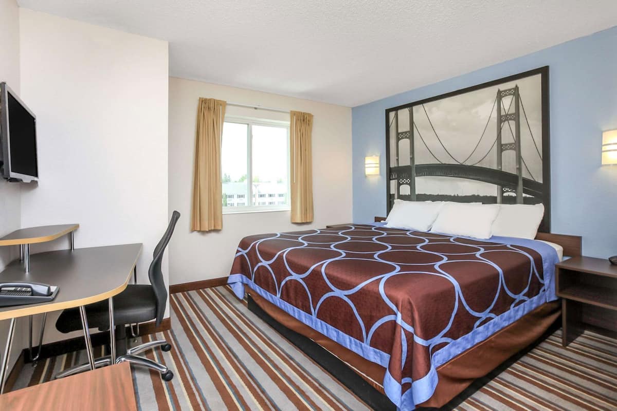 Hotelkamer met een bed, een bureau, een stoel, een raam met gordijnen, een televisie aan de muur en een groot, ingelijst beeld van een brug.