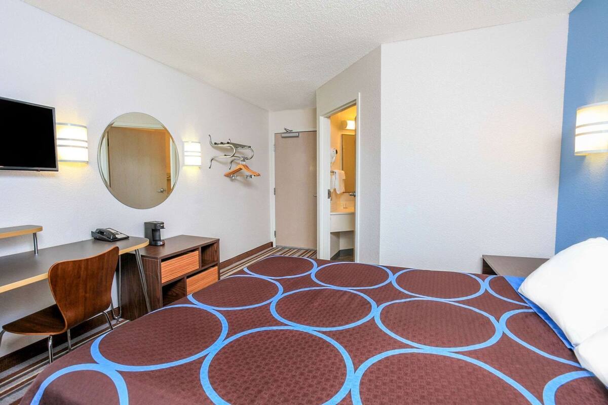 Een hotelkamer met een bed, bureau, stoel, spiegel en een televisie.
