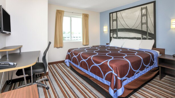 Hotelkamer met een bed, bureau, stoel, televisie, raam met gordijnen en een wandlamp.
