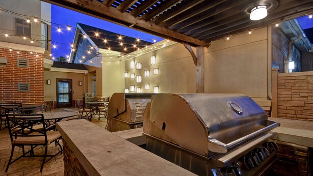 Un patio exterior con una parrilla, mesas, sillas y luces colgantes.