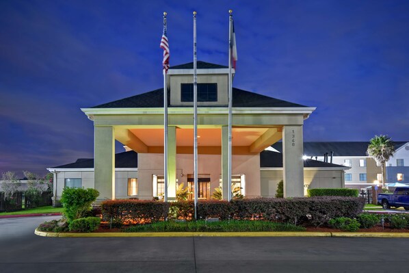 A hotel with a covered entrance, American flags, and a well-maintained garden.