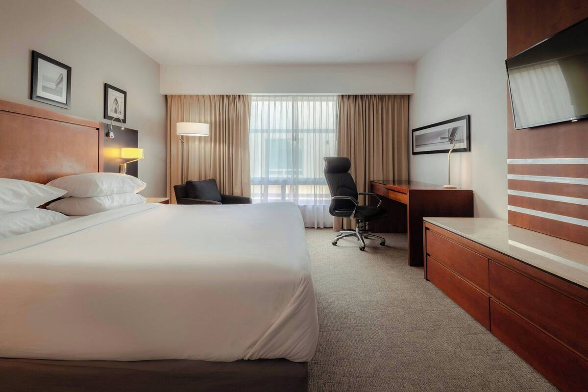 Habitación de hotel con una cama grande, un escritorio, una silla, un televisor y una ventana con cortinas.