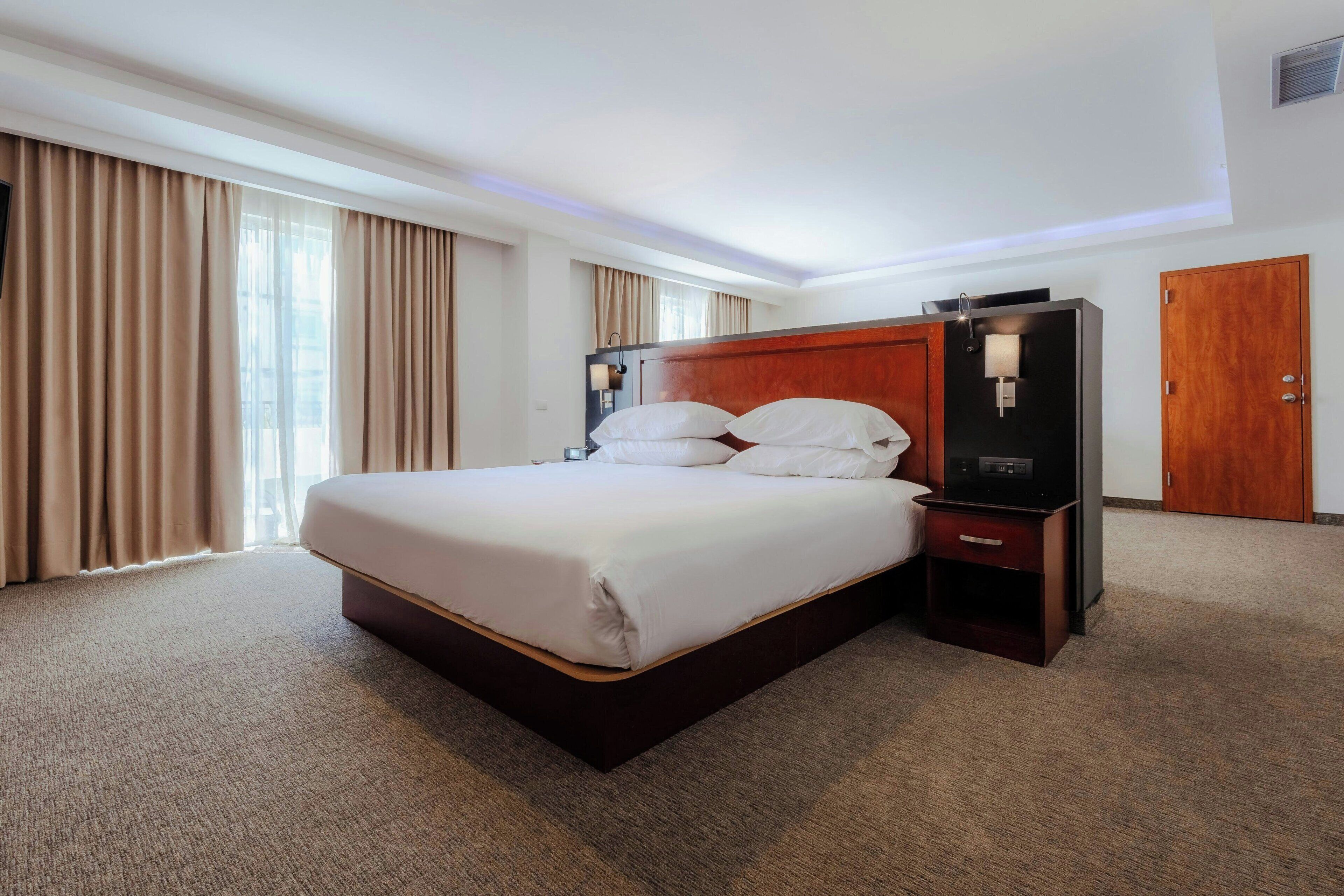 Una habitación de hotel con una cama grande, cabecera de madera, mesita de noche y armario.