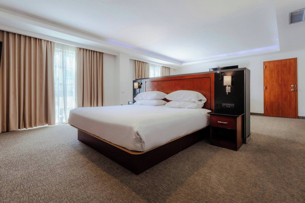 A hotel room with a large bed, a wooden headboard, a bedside table, and a wardrobe.