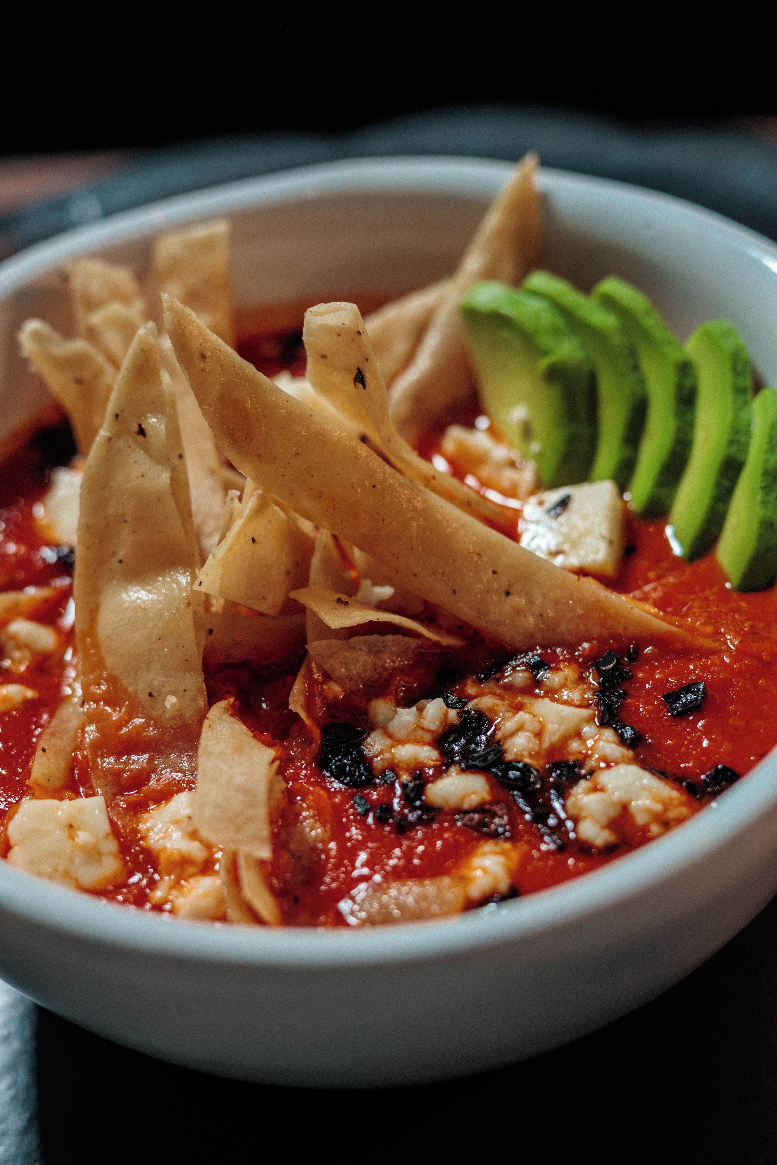 Eine Schüssel Suppe mit Tortilla-Chips und Avocado-Scheiben.