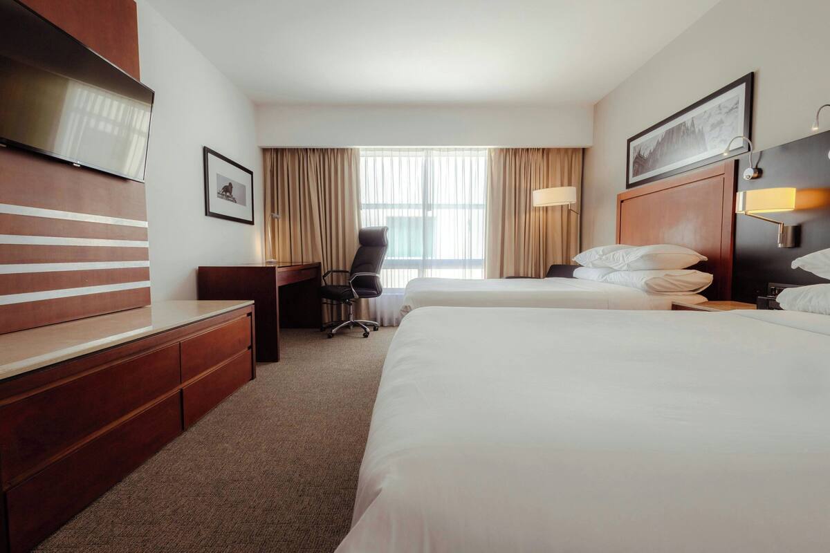 Habitación de hotel con dos camas, un escritorio, una silla, un televisor y una ventana con cortinas.