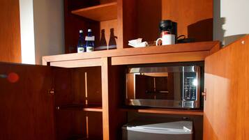 A compact kitchen with a microwave, refrigerator, and wooden shelves.