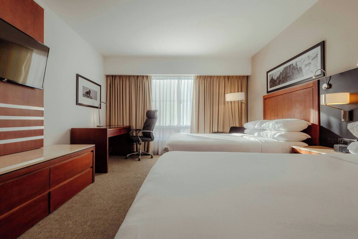 Habitación de hotel con dos camas, un escritorio, una silla, un televisor y una ventana con cortinas.