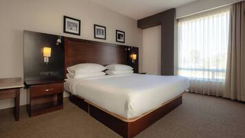 A hotel room with a large bed, two bedside tables, a headboard, and a large window with curtains.