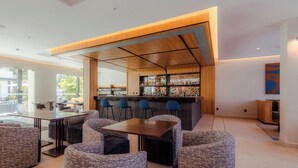 Zona de bar moderna con techo de madera, taburetes y un espacio de estar con sof ás estampados.