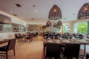 Un comedor amplio con varias mesas dispuestas para los huéspedes, iluminación decorativa en el techo y vistas a zonas verdes al exterior.