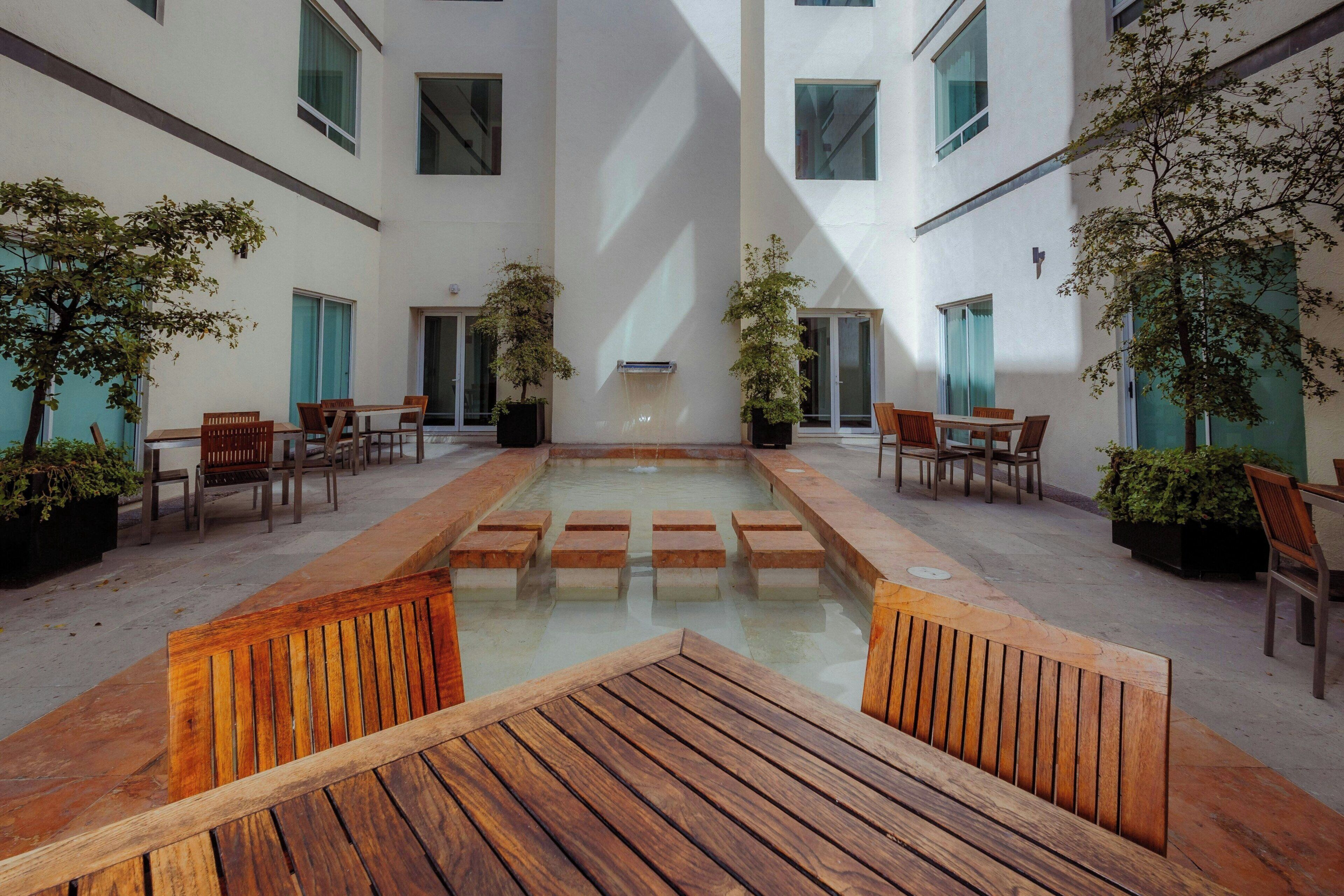 A courtyard with a central water feature, surrounded by wooden benches and chairs, and potted plants.