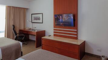 Habitación de hotel con dos camas, un escritorio, una silla, un televisor y un cuadro en la pared.