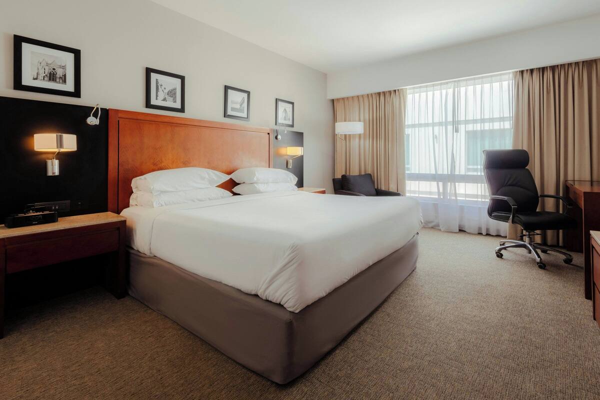 Una habitación de hotel con una cama grande, mesitas de noche, un escritorio y una silla.