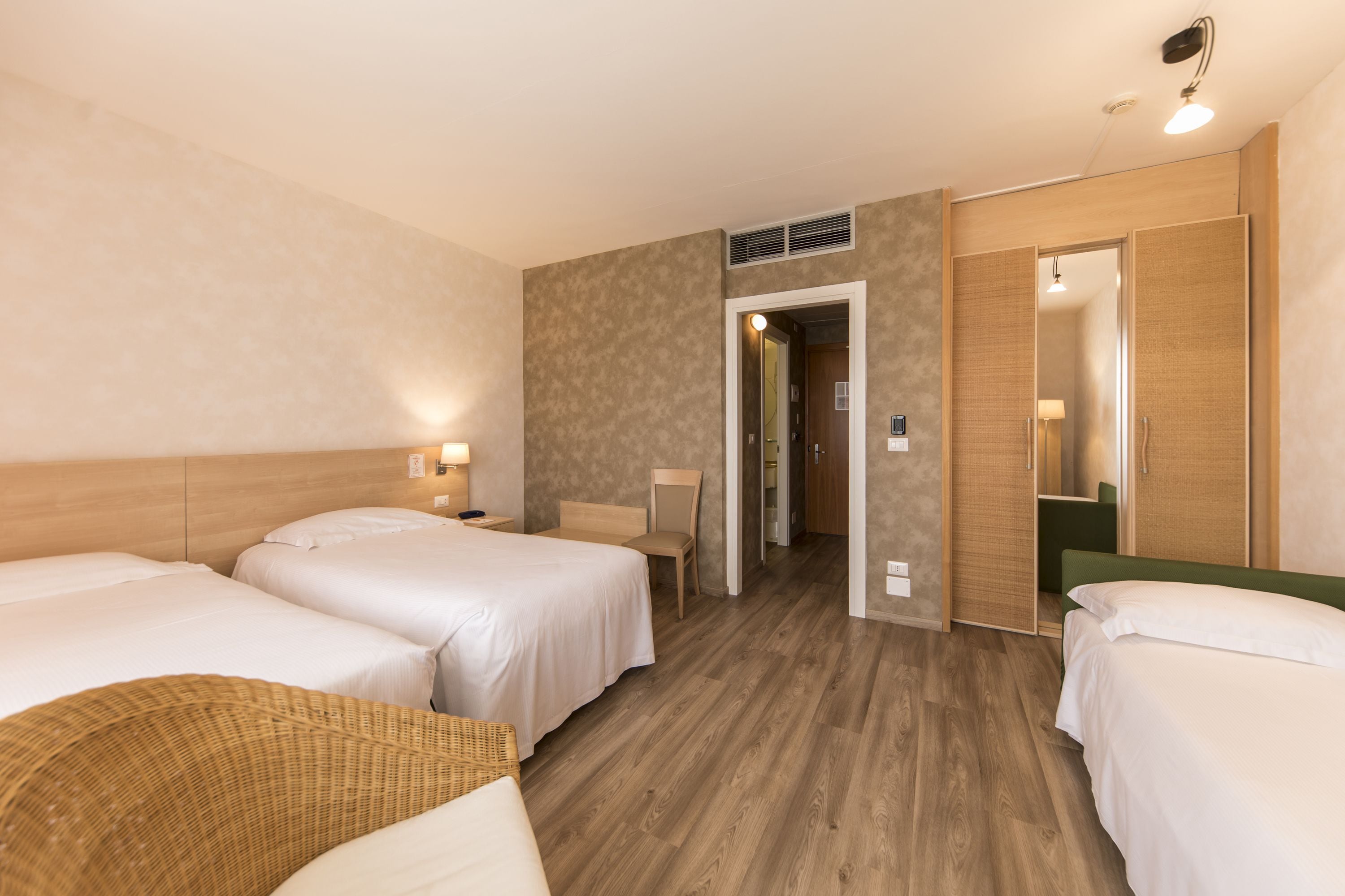 Ein Hotelzimmer mit zwei Betten, einem Sessel, einem Schreibtisch und einem Kleiderschrank.