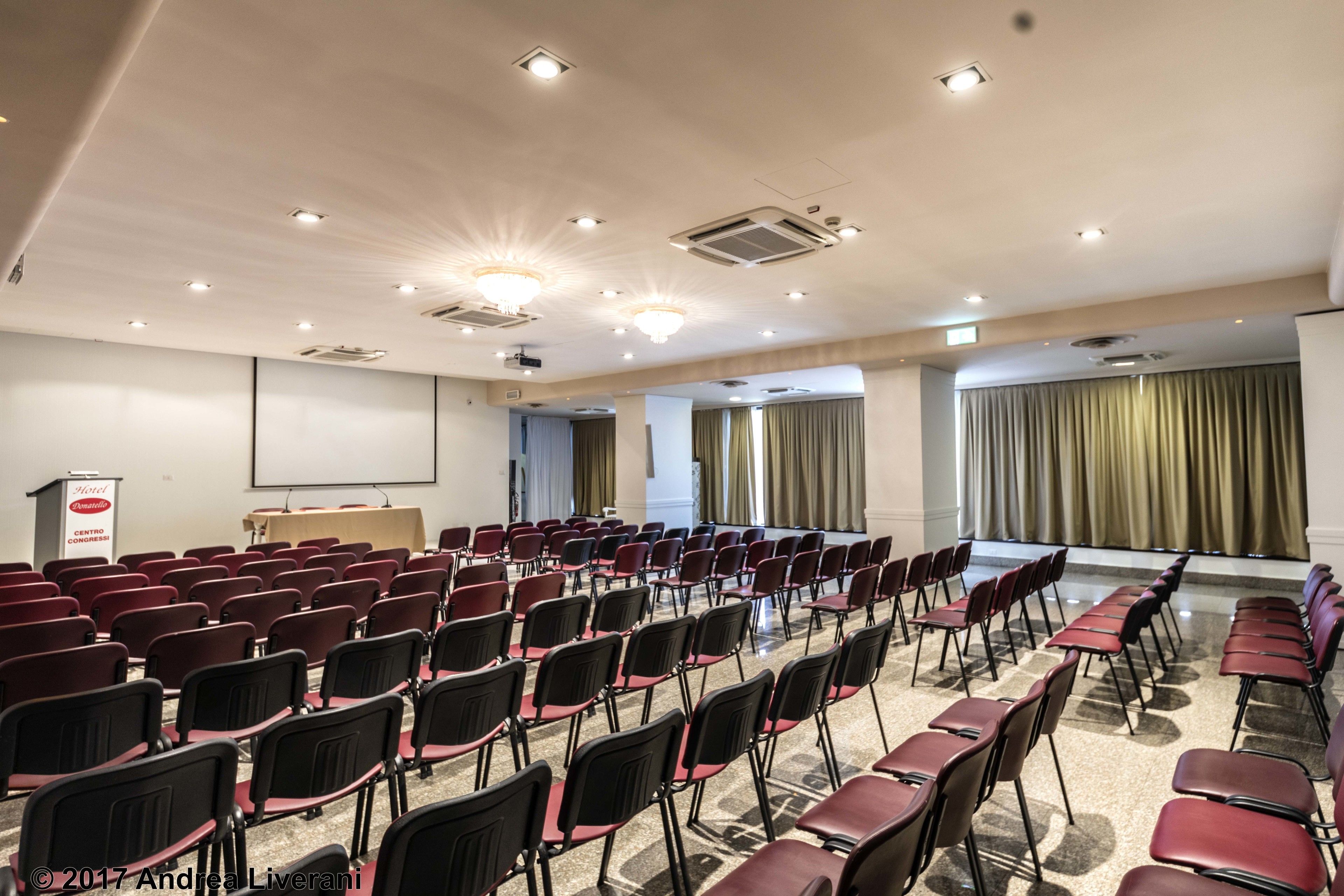A conference room with rows of chairs, a podium, and a projector screen.
