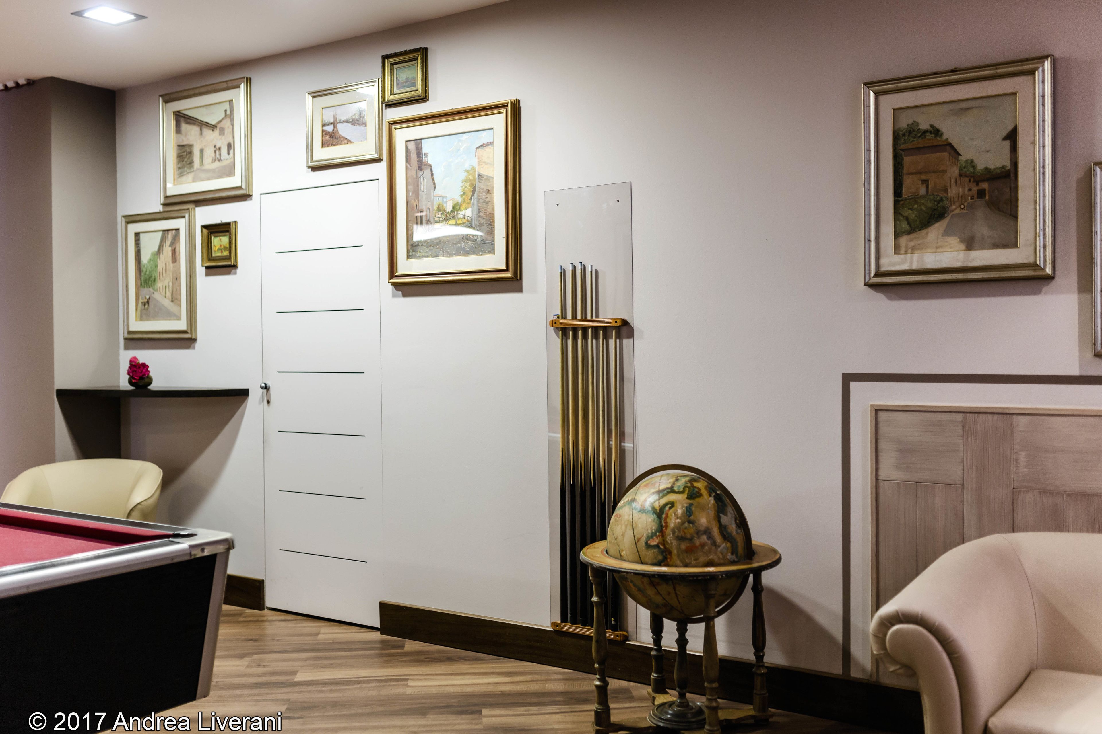 A room with a billiards table, a globe, framed pictures on the wall, and a chair.