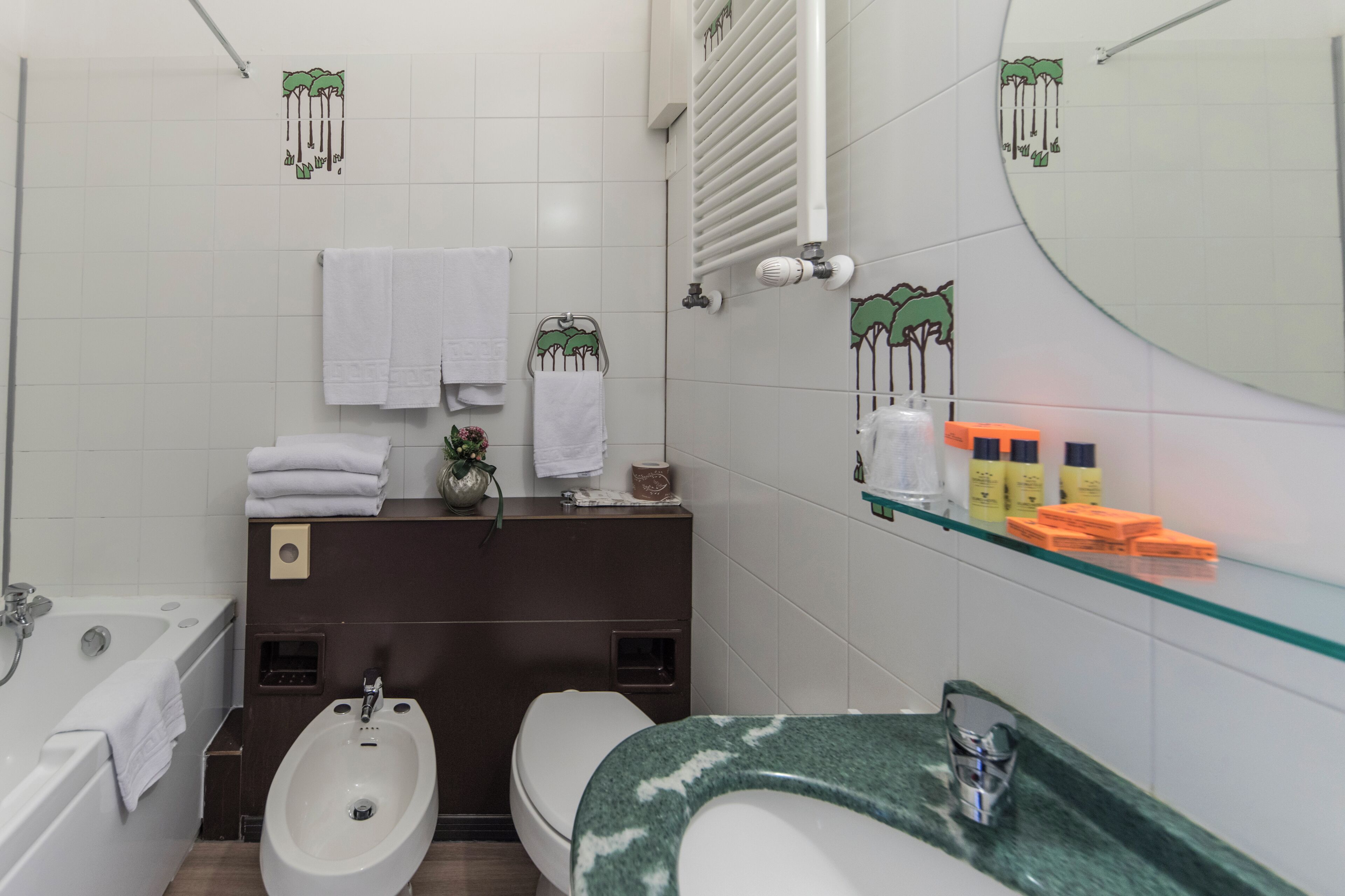Une salle de bain moderne équipée d’une baignoire, d’un bidet, de toilettes et d’une étagère en verre où sont rangés les articles de toilette.