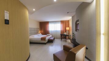 Quarto de hotel com uma cama, uma escrivaninha, uma cadeira e uma pequena mesa com abajur.