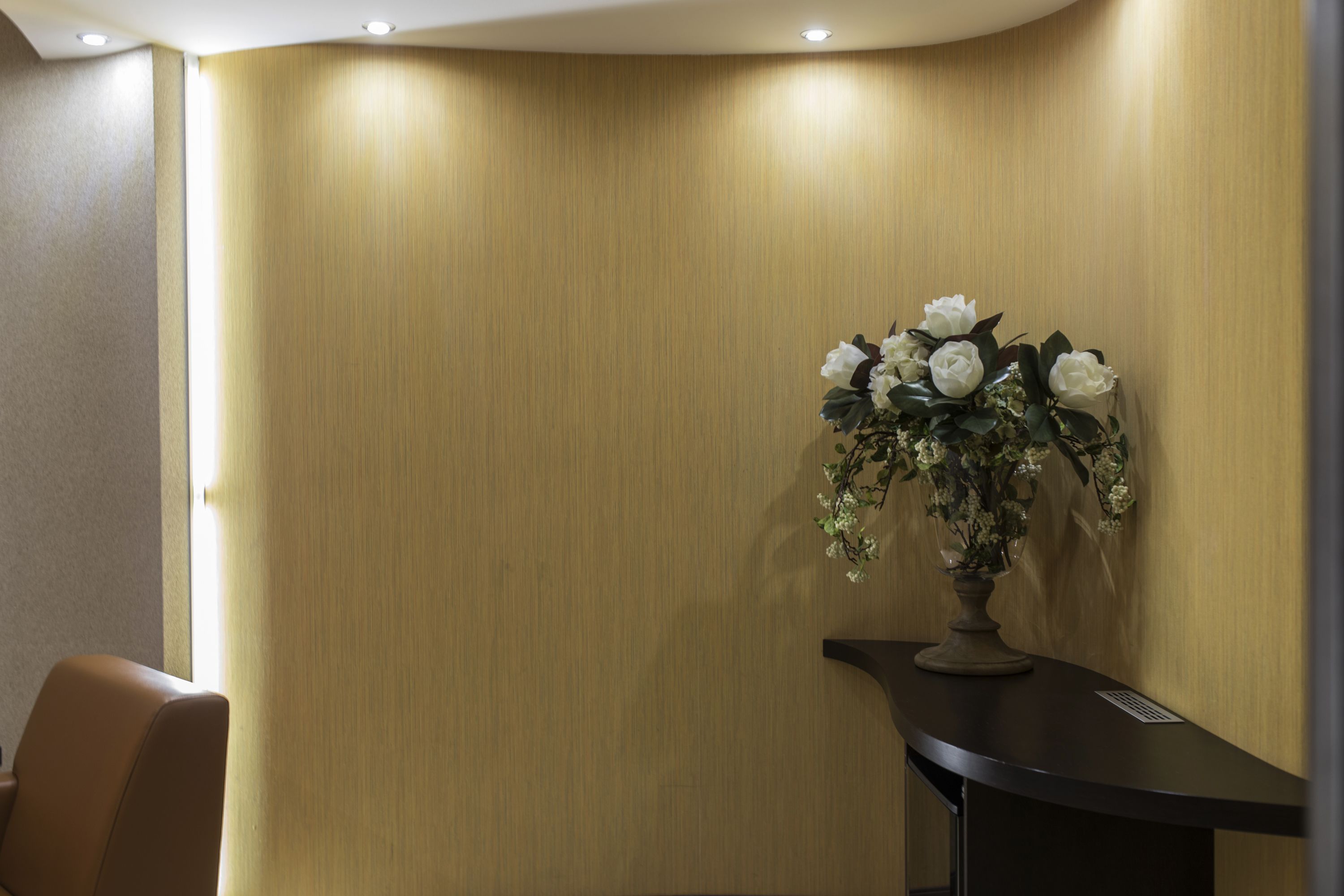 A corner of a room with a wooden wall, a black table with a vase of white flowers, and a brown chair.