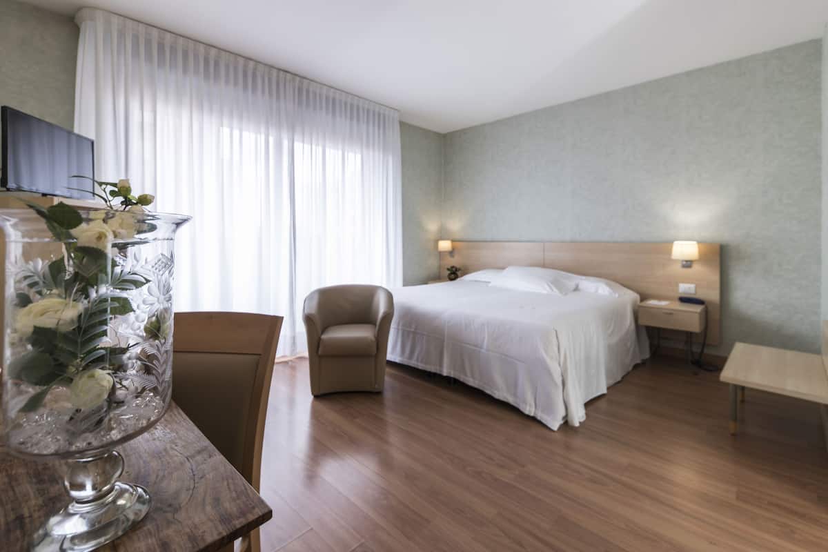 A hotel room with a bed, a chair, a bedside table, a lamp, and a TV on a stand.