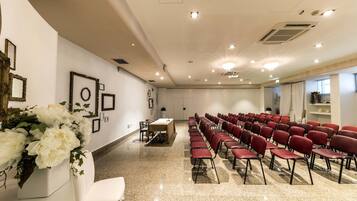 Une salle de conférence avec des rangées de chaises rouges, une table blanche et des tableaux encadrés accrochés aux murs.