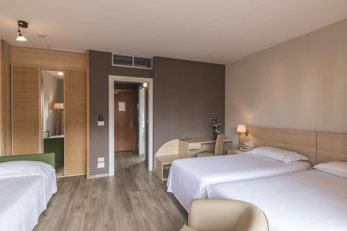 A hotel room with two beds, a desk, a chair, a lamp, and a mirror.