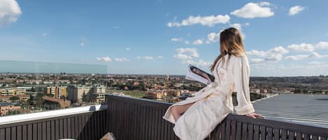 A woman sitting on a balcony with a city view.
