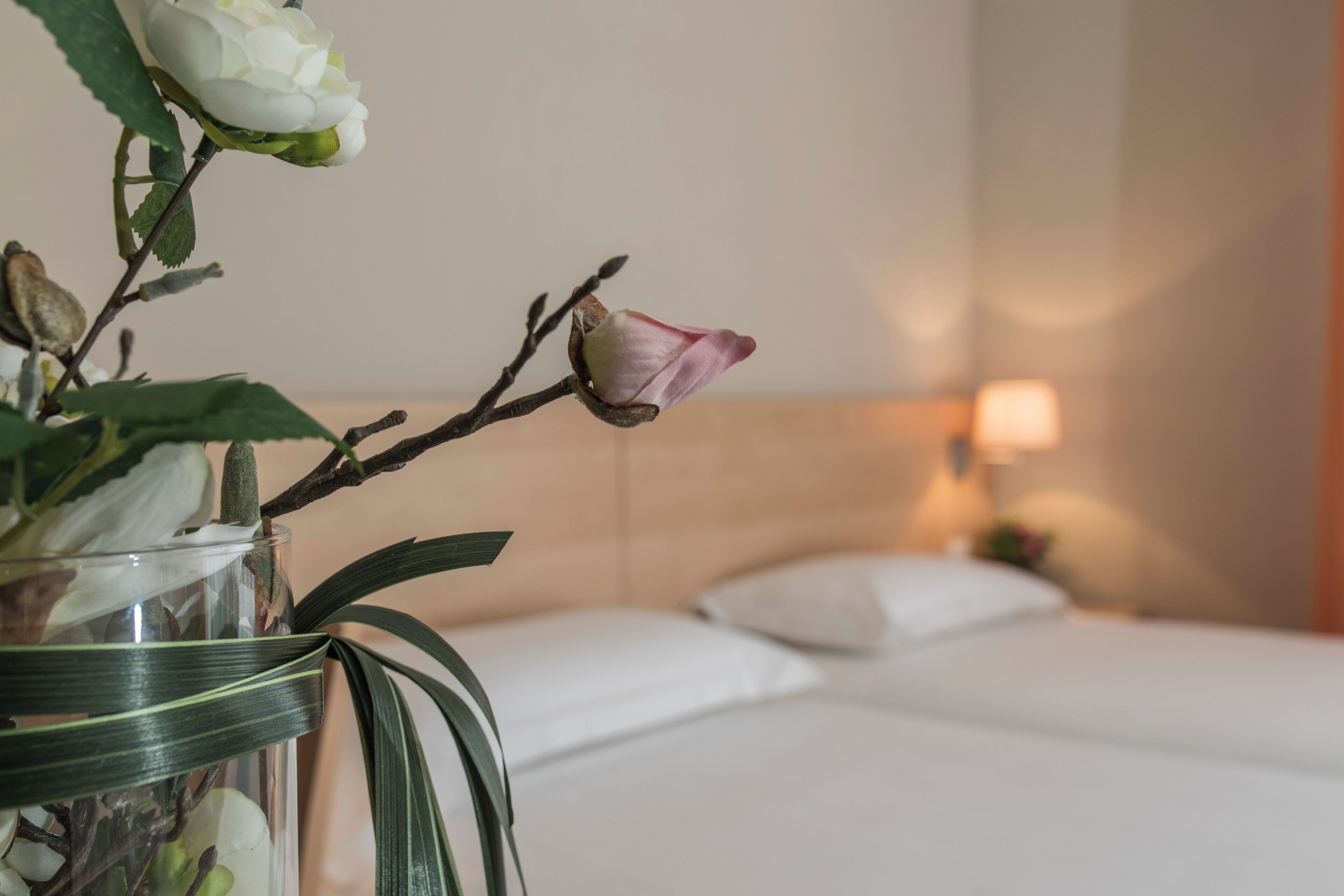 Una habitación de hotel con una cama, una mesita de noche y un jarrón con flores.