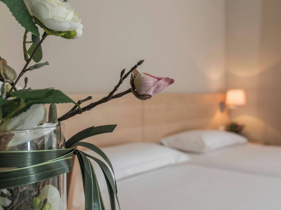 Una habitación de hotel con una cama, una mesita de noche y un jarrón con flores.
